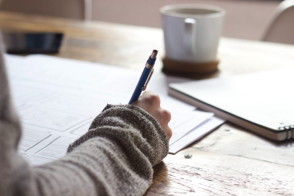 studying some paper laid put with a hand holding a pen and cup